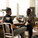 Two men having a casual discussion in a bright indoor setting, highlighting mentorship.