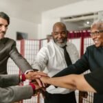 Senior business team showing unity with hands together, diverse colleagues smiling indoors.