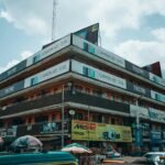 Este prédio incrível no mercado central de Kaduna, na movimentada cidade nigeriana, está iluminado com anúncios irados de celulares Tecno e Camon. Agitação em dias chuvosos com guarda-chuvas abertos e carros passando