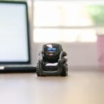 Small toy robot on a desk beside a laptop, symbolizing technology and innovation.