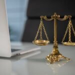 Golden justice scales on a desk beside a laptop, symbolizing law and balance.